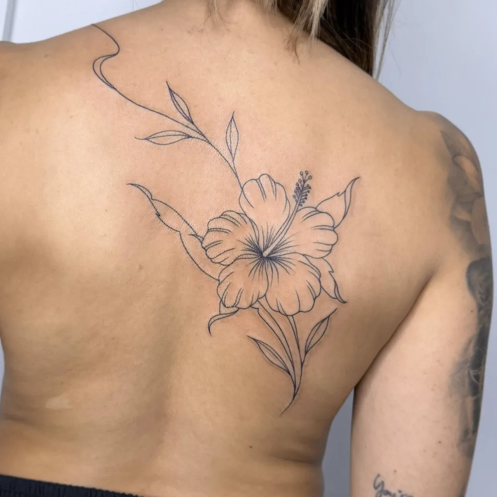 Tatuaje botánico de flor de hibisco en línea fina en la espalda, Chueca, Madrid