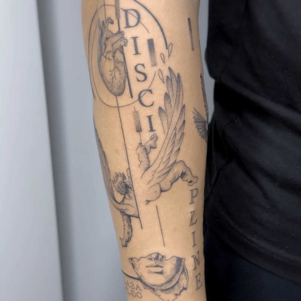 Brazo tatuado con ángeles, corazón anatómico y lettering en microrrealismo, Chueca, Madrid
