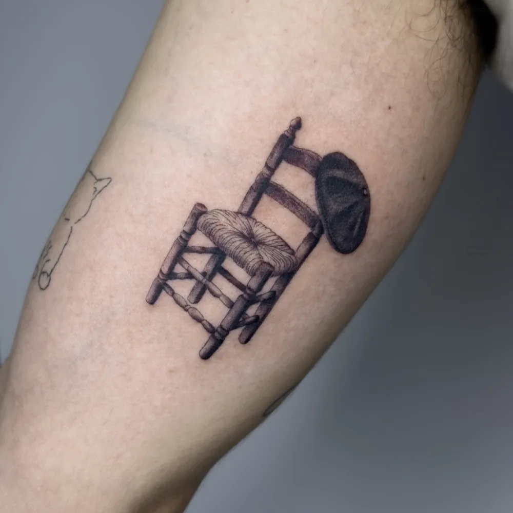 Tatuaje de silla de enea con sombrero en microrrealismo negro y gris en el brazo, Madrid
